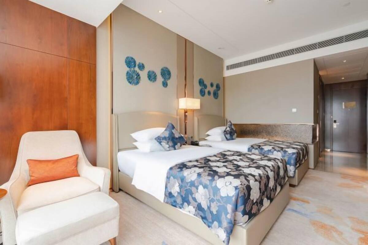 A hotel room with two beds, a chair, a lamp, and decorative wall art.
