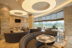 Un rebedor d'hotel modern amb una zona d'aixetes corbada, una taquilla d'informació i grans finestres que ofereixen una vista.