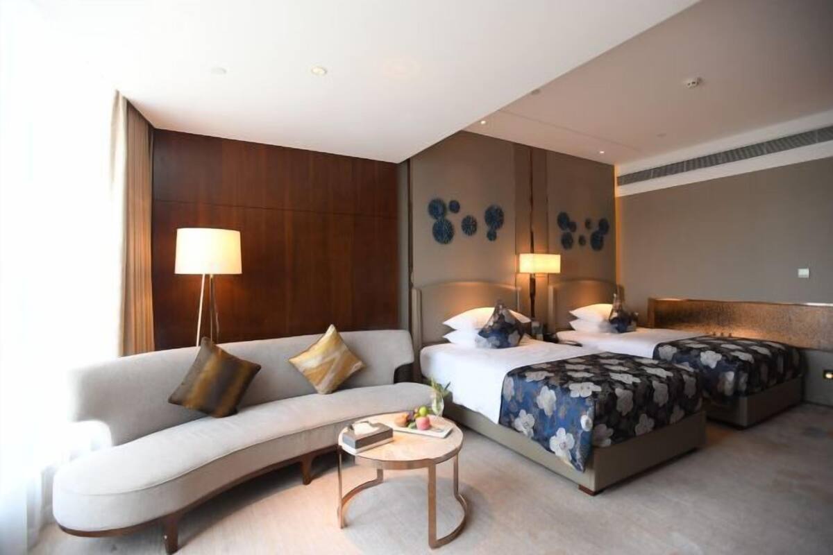 A modern hotel room with a sofa, two beds, a small round table, and wall art.