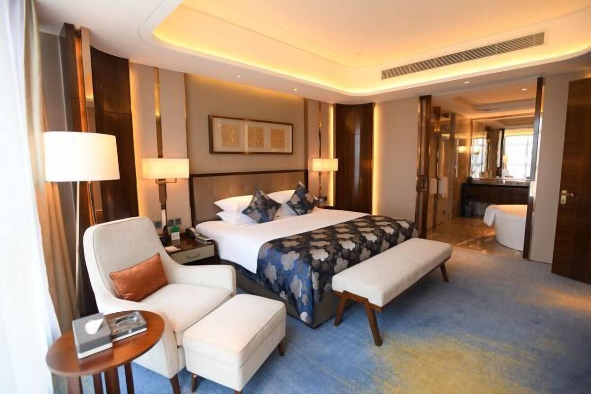 A hotel room with a bed, a chair, a bench, a bedside table, and a lamp.