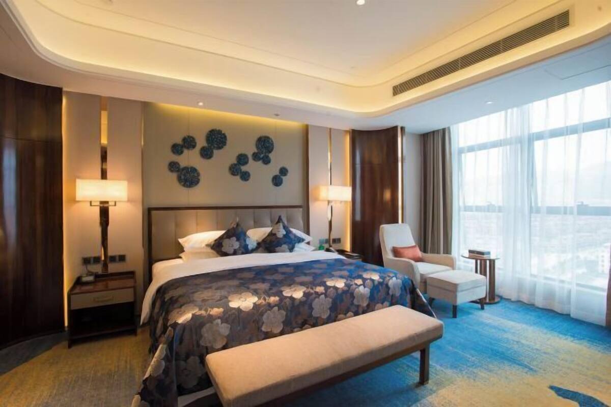 A modern hotel room with a large bed, a bench, a desk, and a chair.