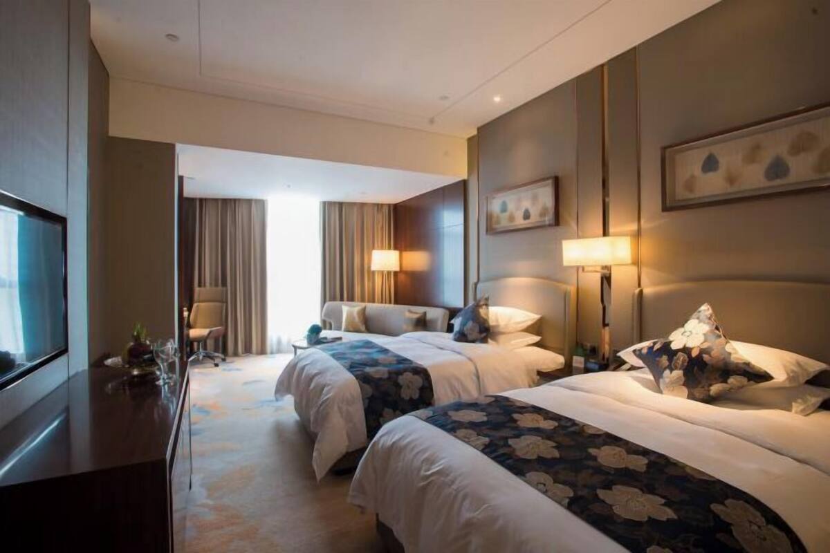 A hotel room with two beds, a desk, a TV, and a window with curtains.