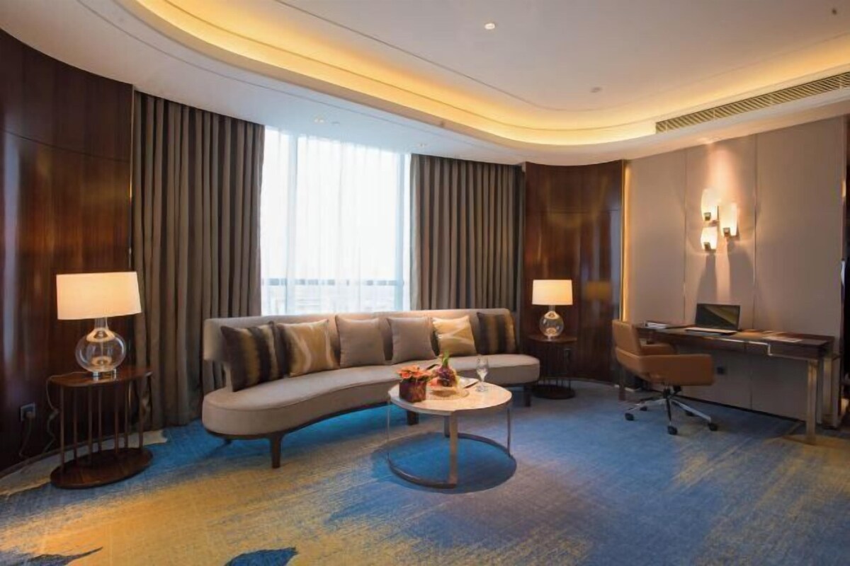 A modern hotel room with a curved sofa, a desk, and a round coffee table.