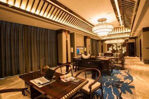 A modern hotel lobby with a wooden reception desk, comfortable seating, a large chandelier, and a blue patterned carpet. - Phoenix Hotel (Wenshan City)