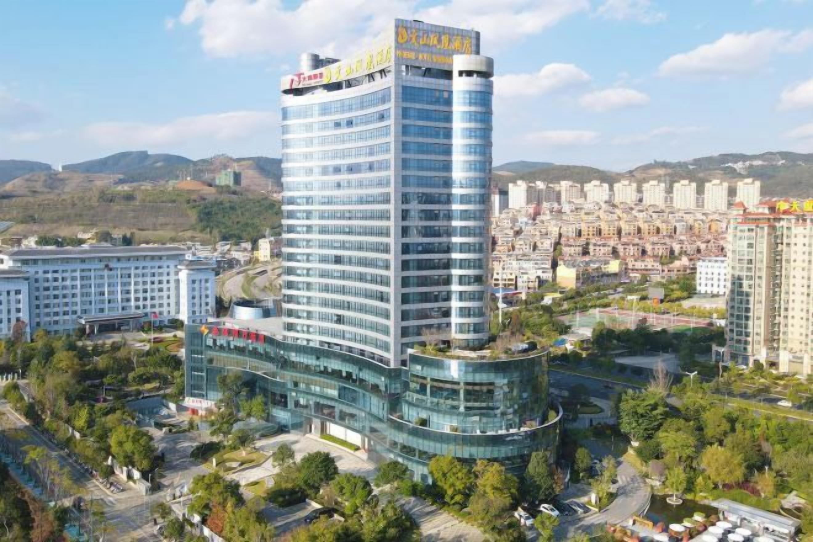 A multi-story hotel with a prominent sign at the top, surrounded by greenery and other buildings.