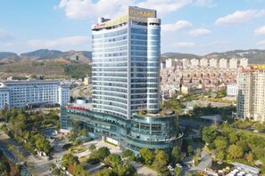 Un hotel de diverses plantes amb un rètol destacat a la part superior, envoltat de vegetació i altres edificis.