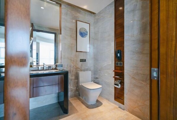 A modern bathroom with a marble wall, a toilet, a sink with a mirror, and a wooden door. - Phoenix Hotel (Wenshan City)