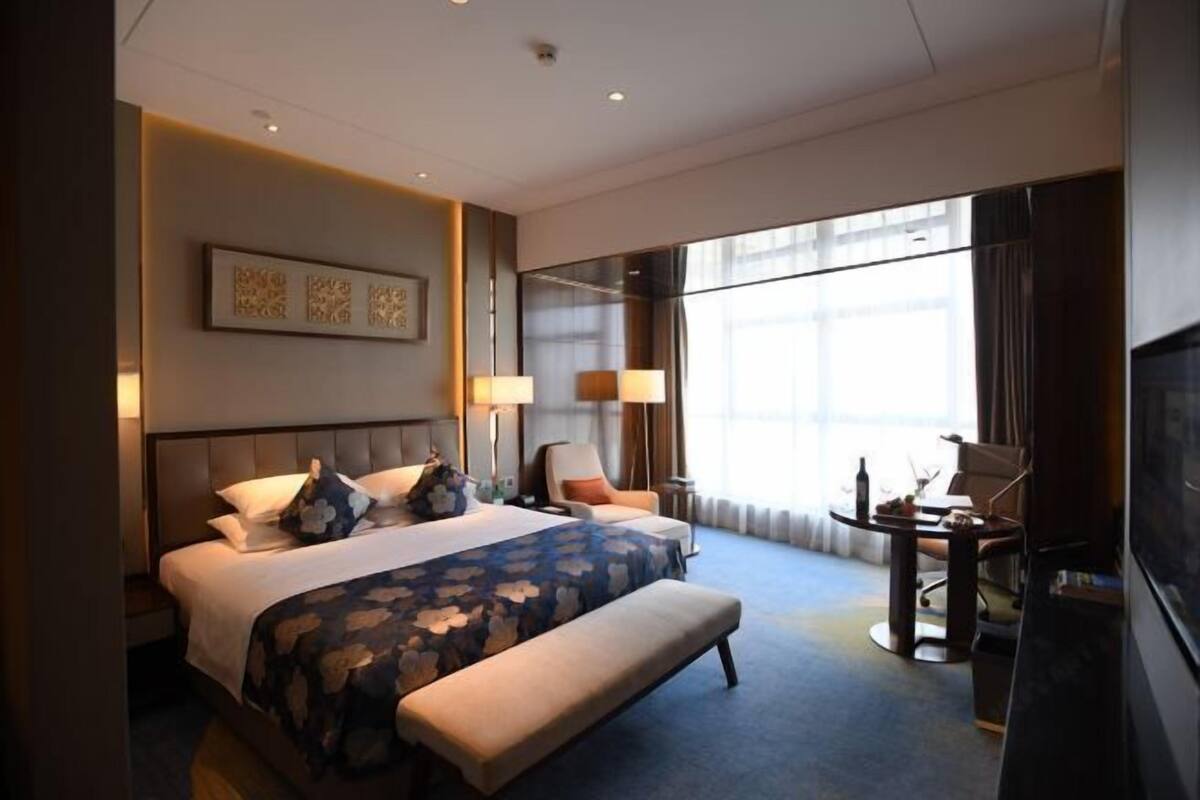 A hotel room with a large bed, a bedside table, a chair, a desk, and a TV.