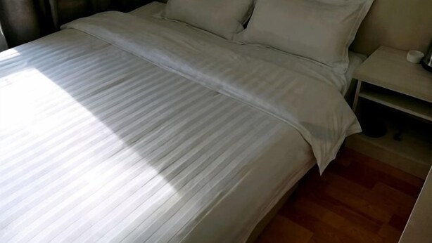 A neatly made bed with a striped bedspread, a bedside table with a lamp, and a wooden floor. - Wanluoyuan Theme Hotel (Antu)