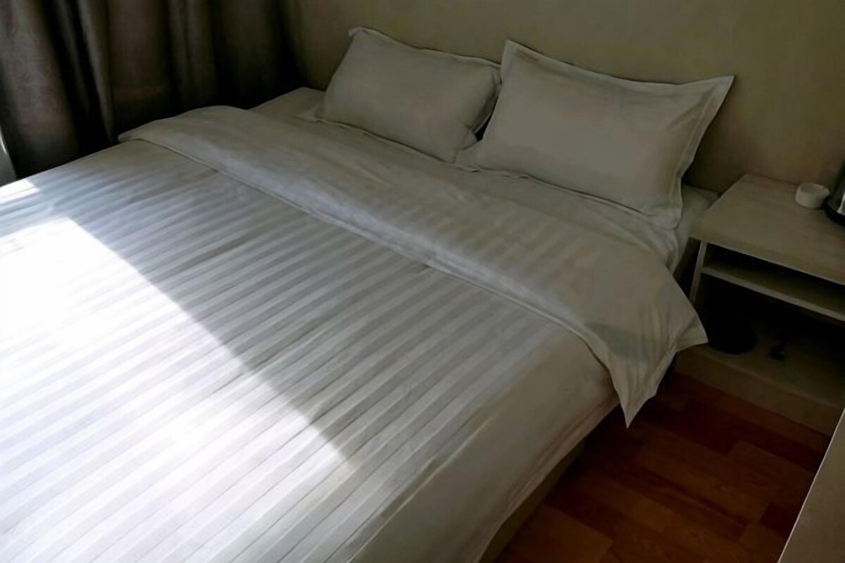 A neatly made bed with a striped bedspread, a bedside table with a lamp, and a wooden floor.