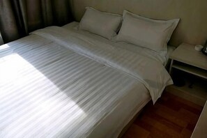 A neatly made bed with a striped bedspread, a bedside table with a lamp, and a wooden floor. - Wanluoyuan Theme Hotel (Antu)