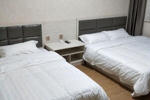 A hotel room with two single beds, a nightstand with a remote control, and a wooden floor.