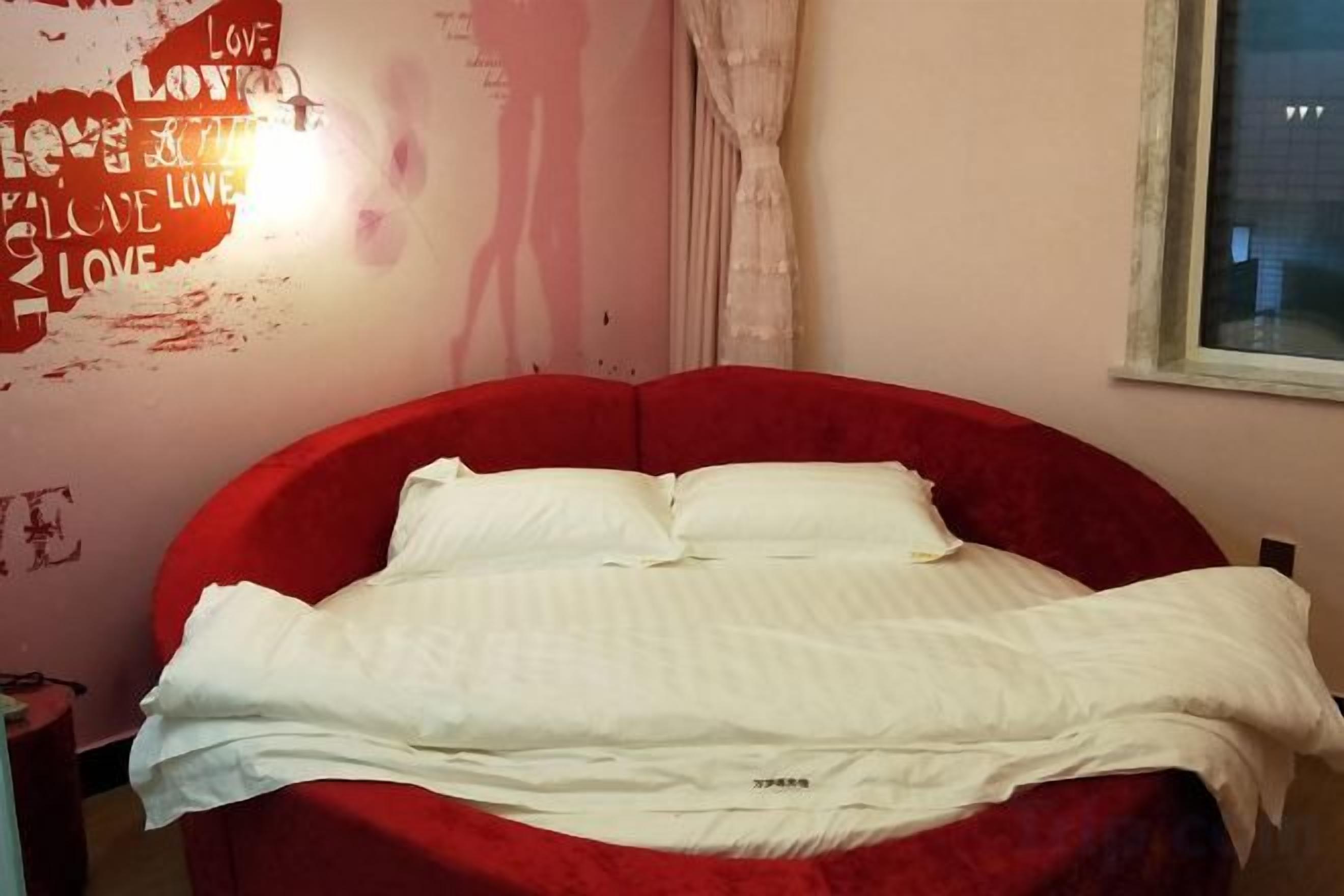 Une chambre avec un lit rouge, du linge de lit blanc et un mur orné de texte et d’un luminaire.