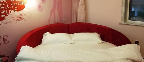 Une chambre avec un lit rouge, du linge de lit blanc et un mur orné de texte et d’un luminaire.