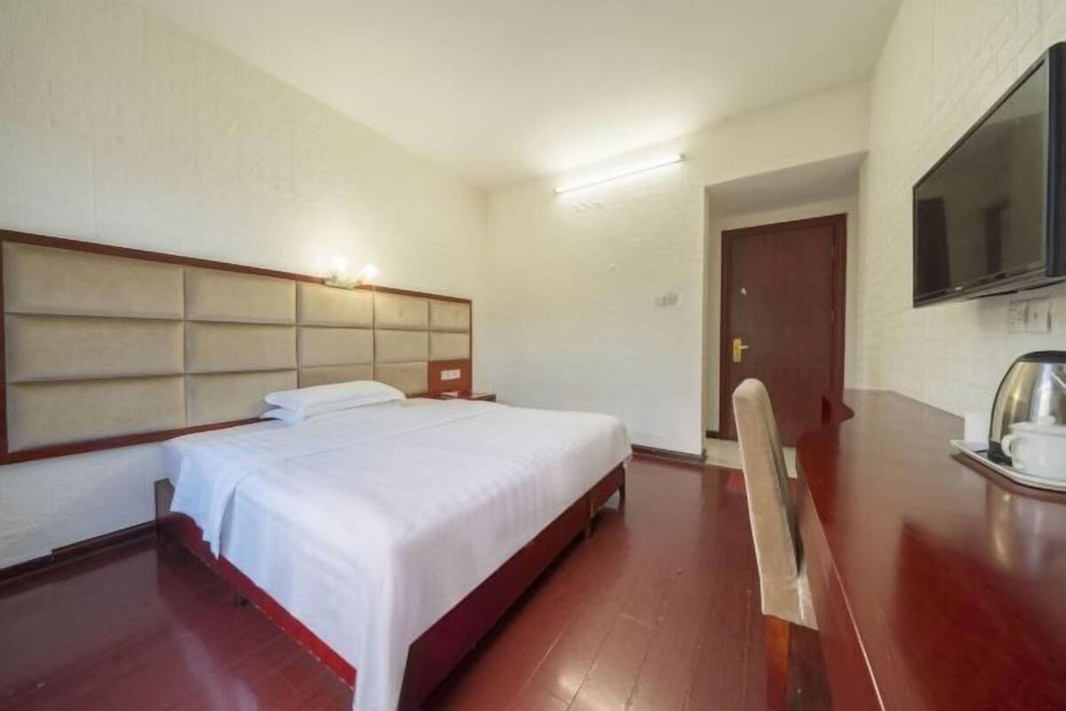 Ett hotellrum med en säng, en sänggavel i trä, en tv som är monterad på väggen och ett träbord med ett bricka.