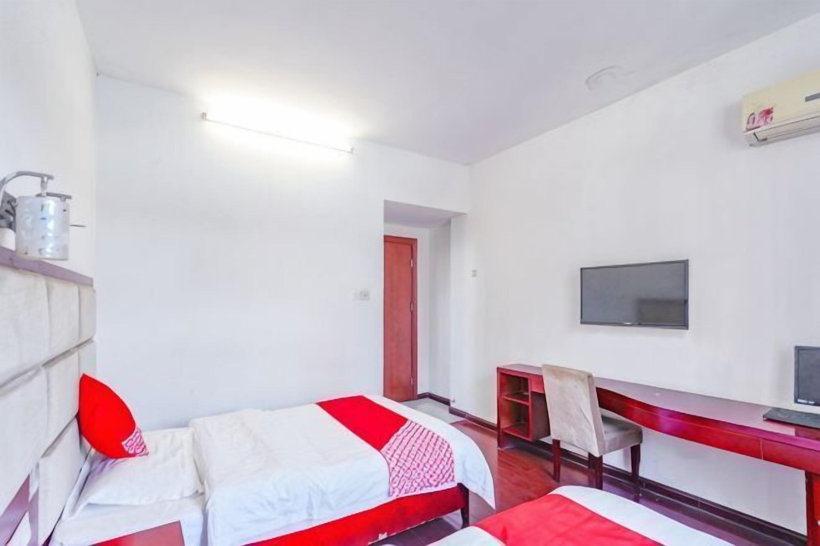 Habitación de hotel con dos camas, un escritorio, una silla, un televisor y una puerta roja.