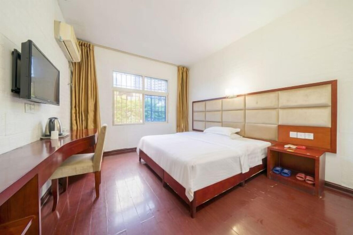 A hotel room with a bed, a desk, a chair, a TV, and a window.