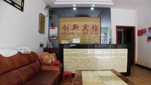A reception area with a wooden sign, a brown leather sofa, a small stool, and a marble-patterned table. - Cangzhou Innovation Hotel (Cangzhou West Railway Station Star School Branch) (Chenzhou)