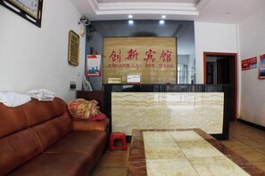 A reception area with a reception desk, a brown sofa, a small red stool, and a wall-mounted sign. - Cangzhou Innovation Hotel (Cangzhou West Railway Station Star School Branch) (Chenzhou)