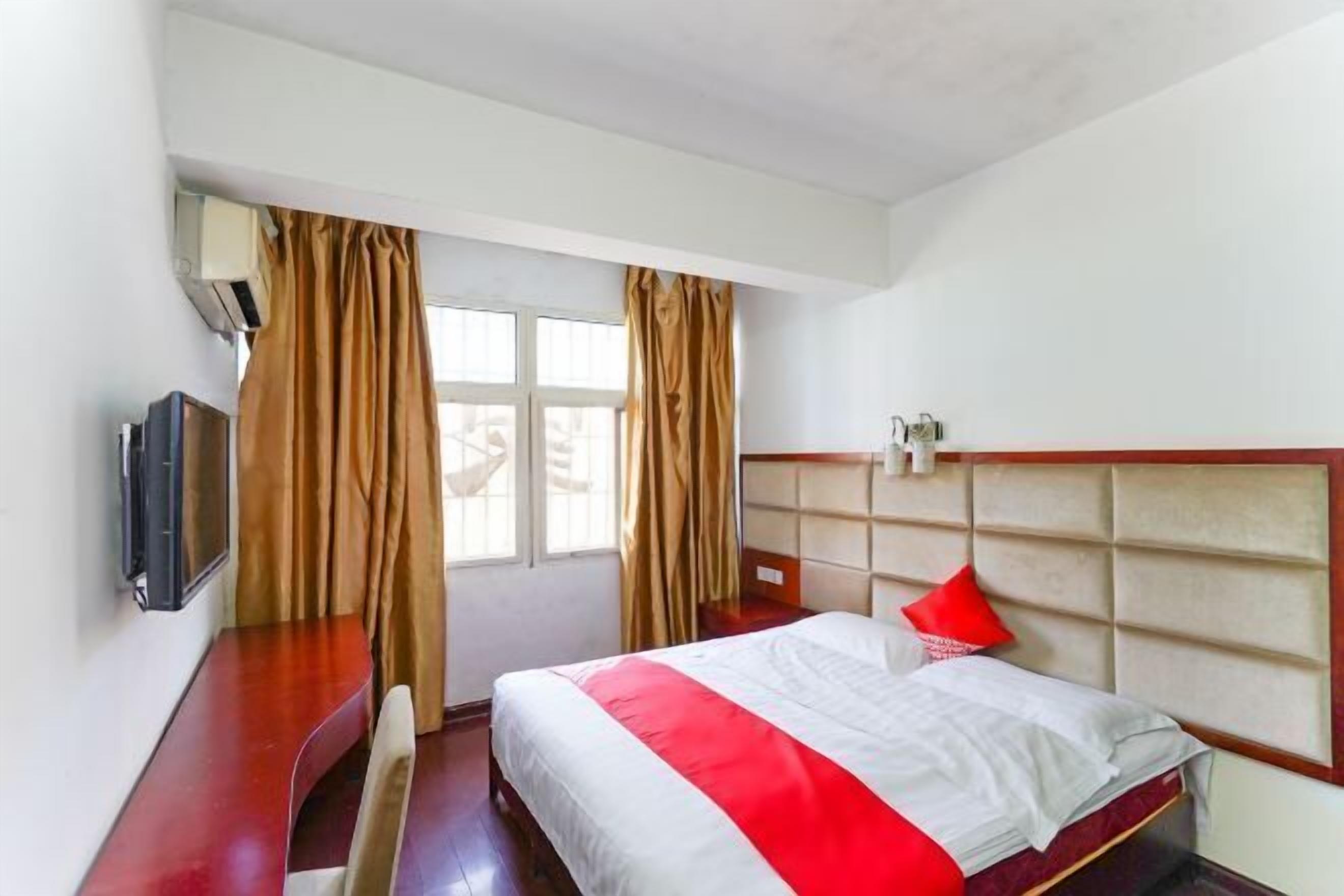 Een hotelkamer met een bed, een bureau, een stoel, een televisie en een raam met gordijnen.