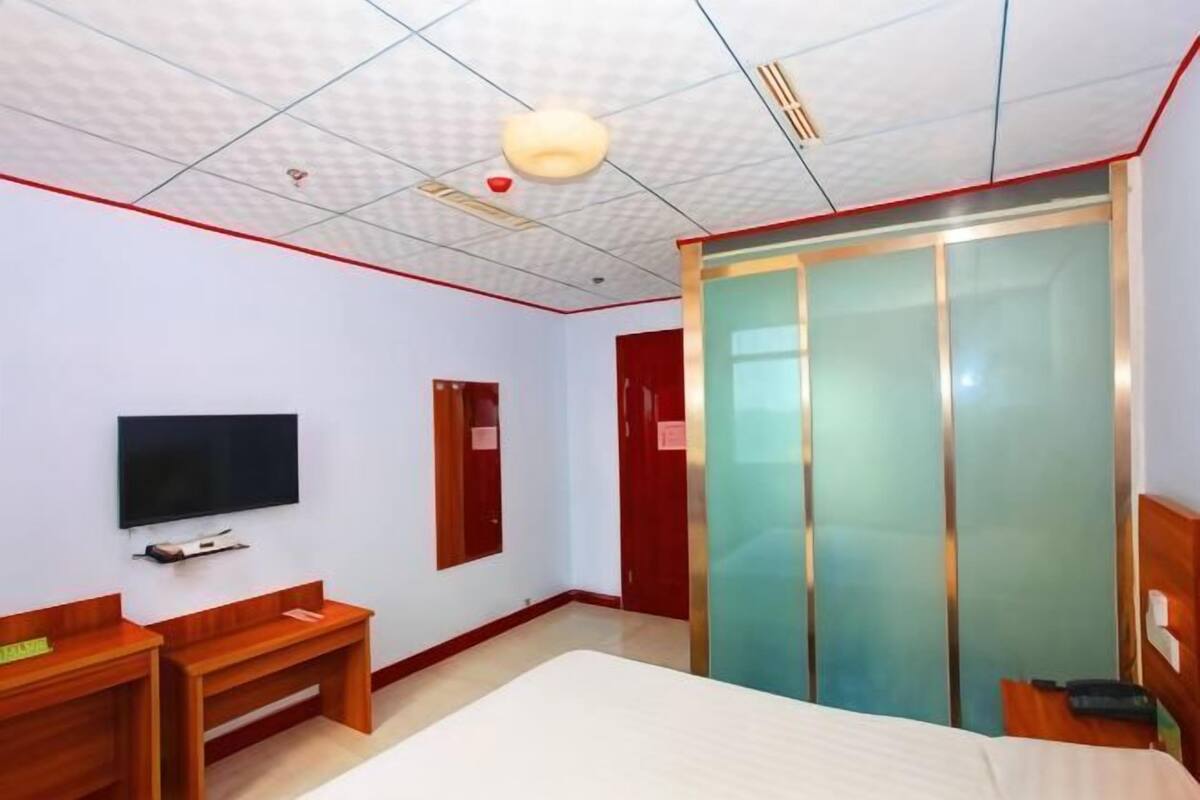 Ett hotellrum med en säng, en tv, ett skrivbord, en garderob och en skjutdörr.