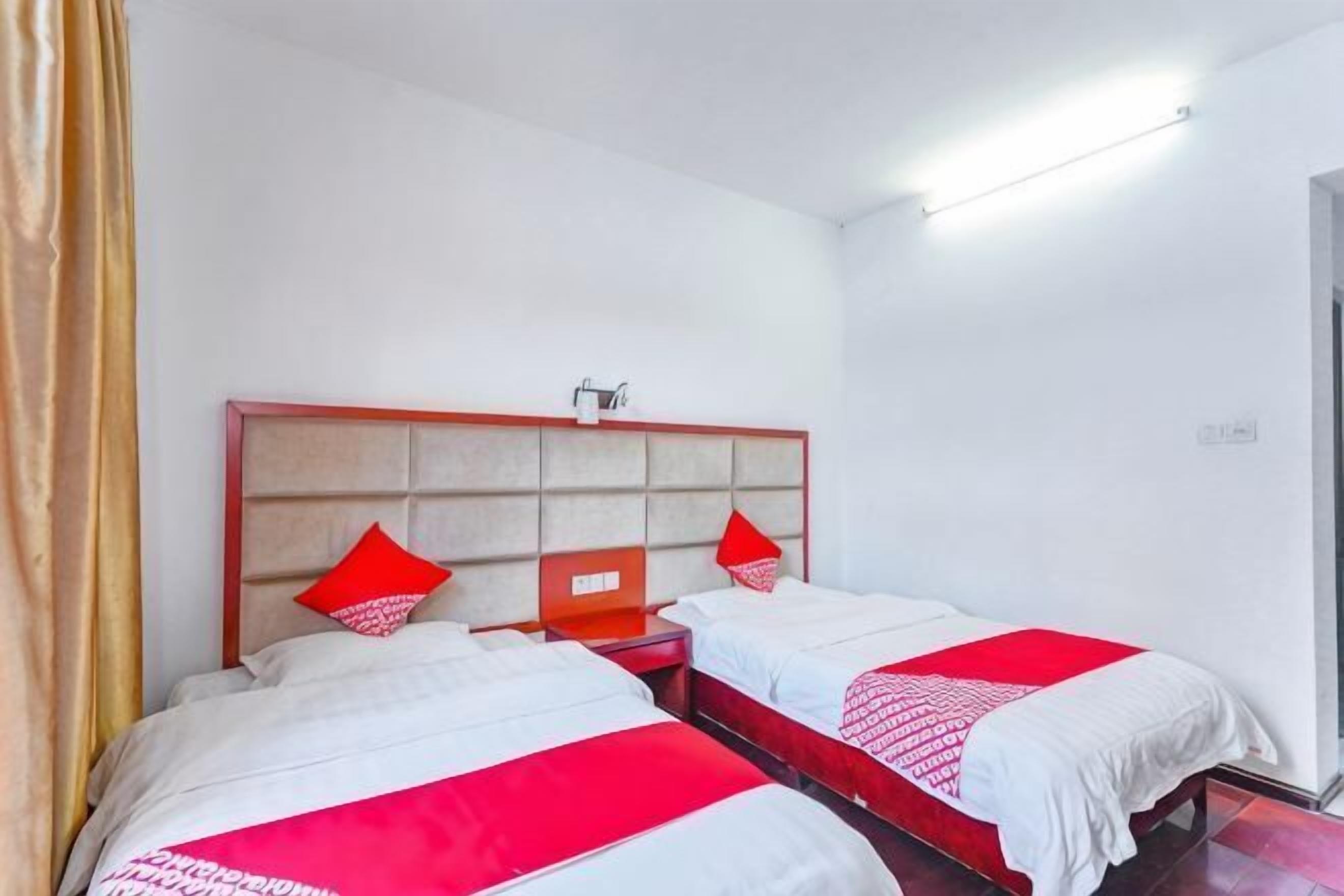 Een hotelkamer met twee bedden, een rood hoofdeinde, wit beddengoed en een rode decoratieve kussen.