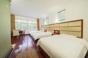 Habitación de hotel con tres camas, zona de comedor y ventanas amplias.