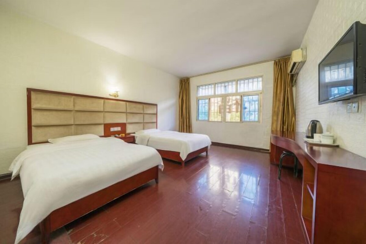 A hotel room with two beds, a wooden headboard, a desk, a chair, a television, and a window with curtains.