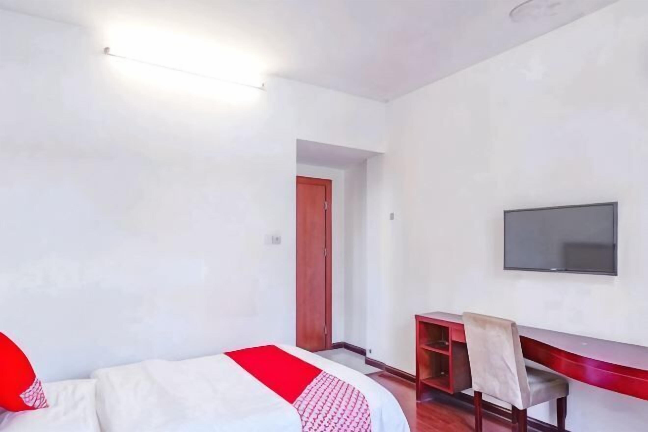 A hotel room with a bed, a desk, a chair, a television, and a door.