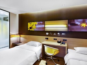 Ett hotellrum med två sängar, ett skrivbord, en stol och en TV som är monterad på väggen.