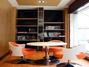A modern room with a round table, two orange chairs, a bookshelf, and a window. - 7 Days Inn Guilin Central Plaza (Guilin)