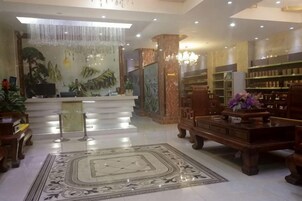 Un vestíbulo de hotel con una recepción, un tapete decorativo grande y un área de estar con una mesa y sillas de madera.