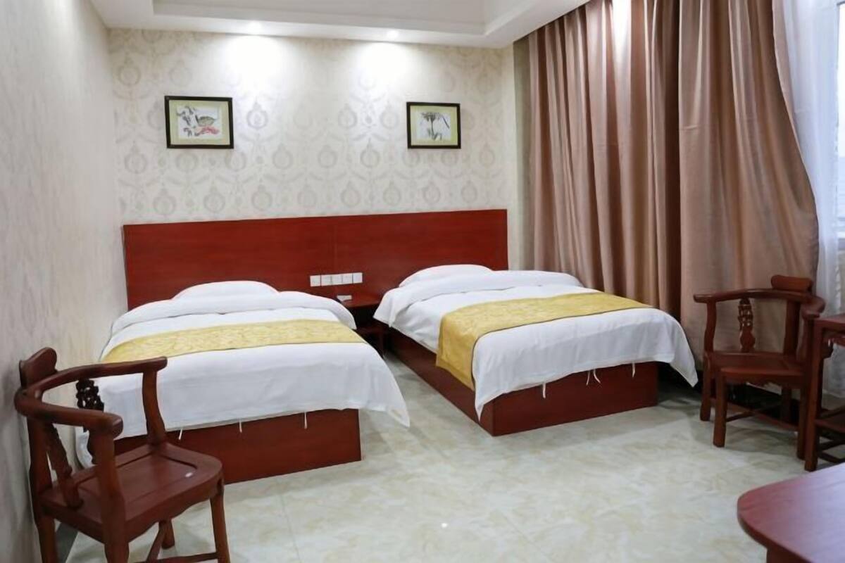 Habitación de hotel con dos camas, cabecero de madera, escritorio y sillas.