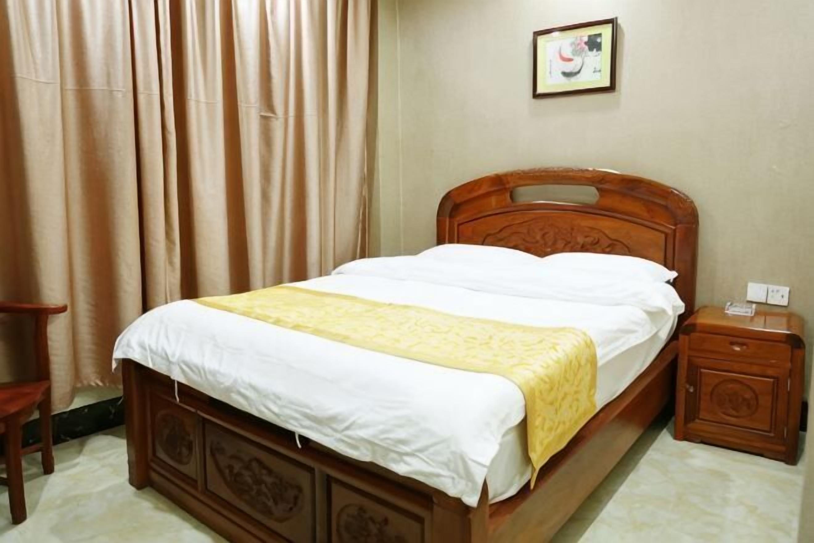 A wooden bed with a white and yellow bedspread, a nightstand, a chair, and a framed picture on the wall.