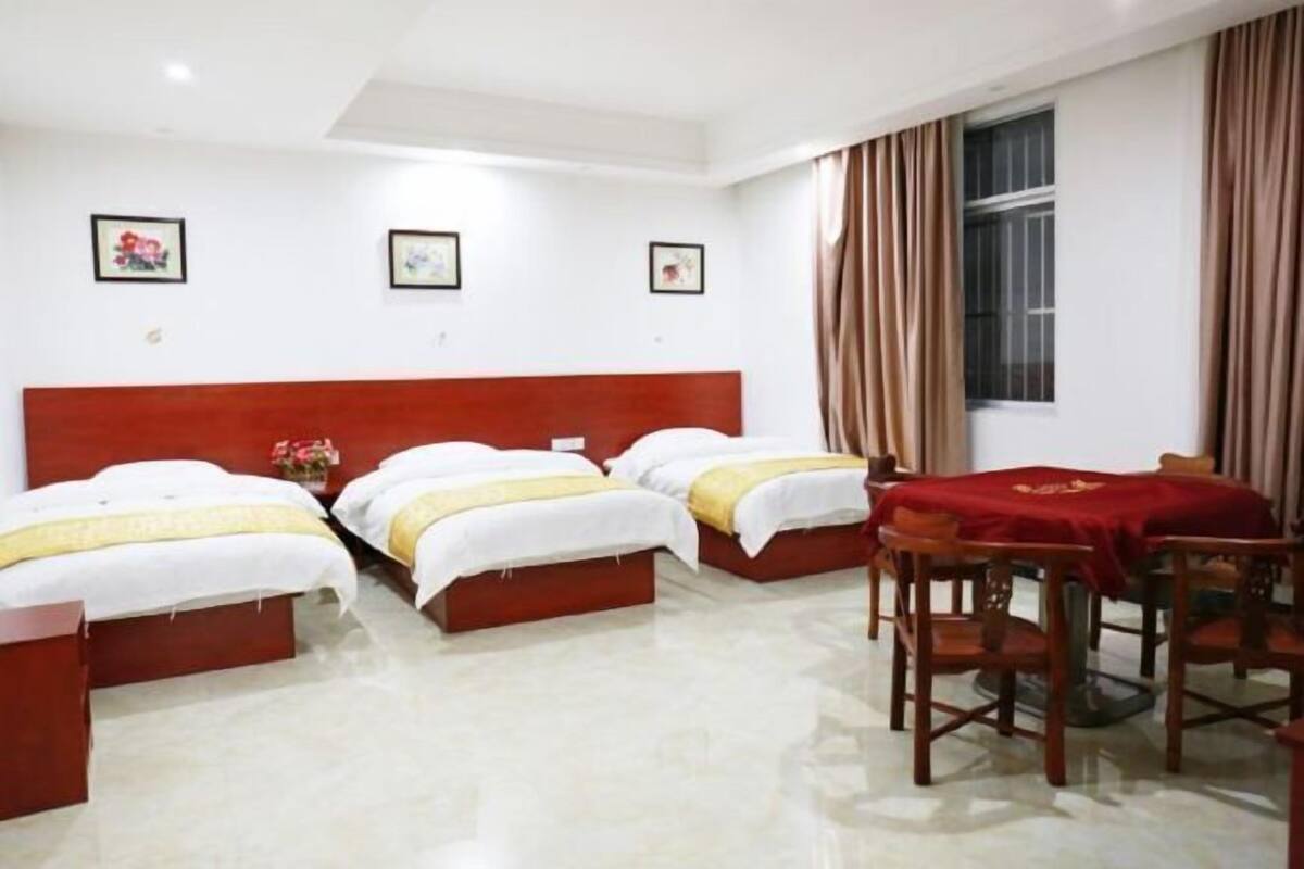 Una habitación de hotel con tres camas, una mesa de comedor con sillas y una ventana con cortinas.