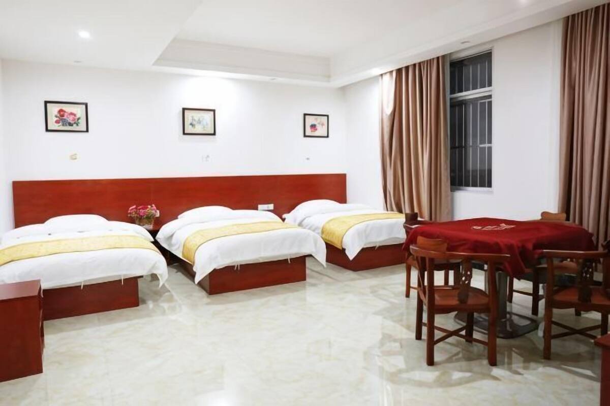 Una habitación de hotel con tres camas, una mesa de comedor y un ventanal con cortinas.