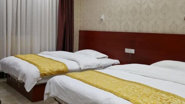 A hotel room with two beds, a wooden headboard, a patterned wall, and a window with curtains. - Pingxiang IKEA Hotel Apartment (Pingxiang)
