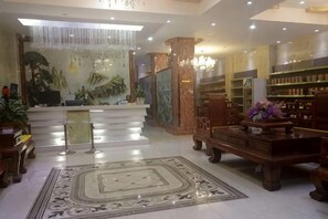 A hotel lobby with a reception desk, a large decorative rug, and a bookshelf with various items. - Pingxiang IKEA Hotel Apartment (Pingxiang)