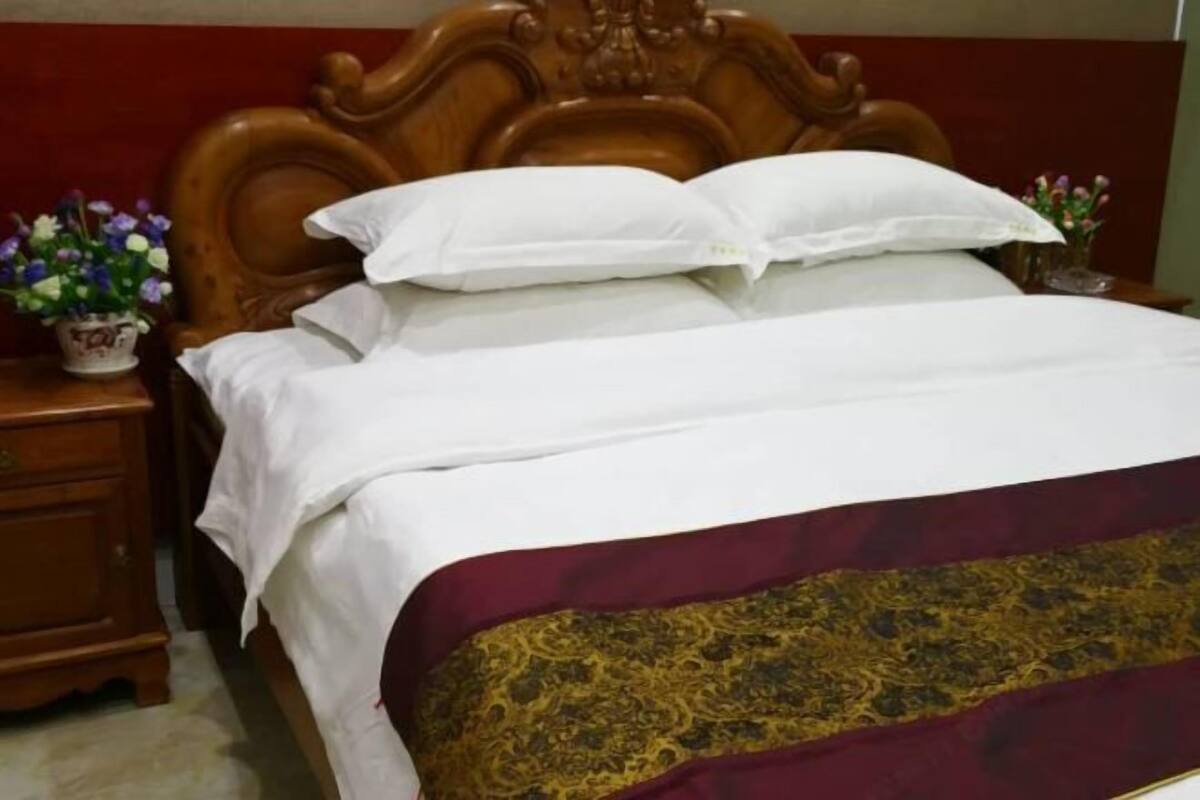 Una cama con cabecera de madera, ropa de cama blanca y una colcha de cuadros en tonos granate y dorado.