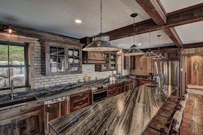 A kitchen with a long island, wooden cabinets, and hanging pendant lights.