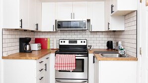 Una cocina compacta con armarios blancos, microondas, estufa y fregadero.