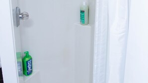 Ducha blanca con cabezal de ducha de mano, una botella de champú y cortina de baño.