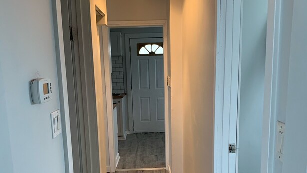 Un pasillo con piso de madera, paredes blancas y una puerta que da a una cocina.