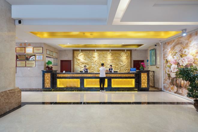 A reception area with a marble floor, a reception desk with a golden back panel, framed certificates on the wall, and a floral mural.