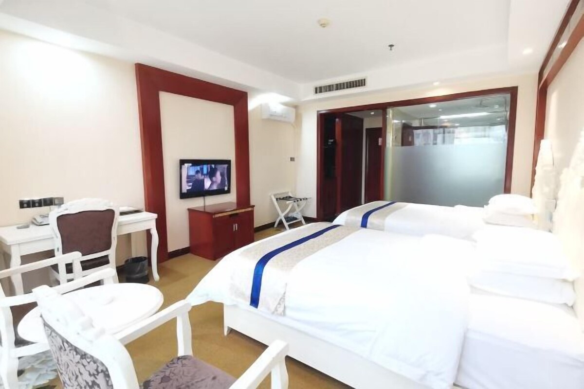 A hotel room with two beds, a desk, a chair, a TV, and a wardrobe.