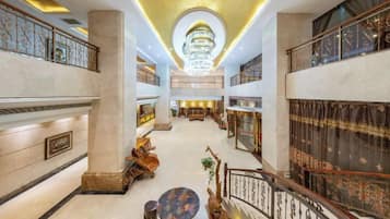 Un amplio vestíbulo de hotel con una imponente araña, varias zonas de estar y una escalera central.