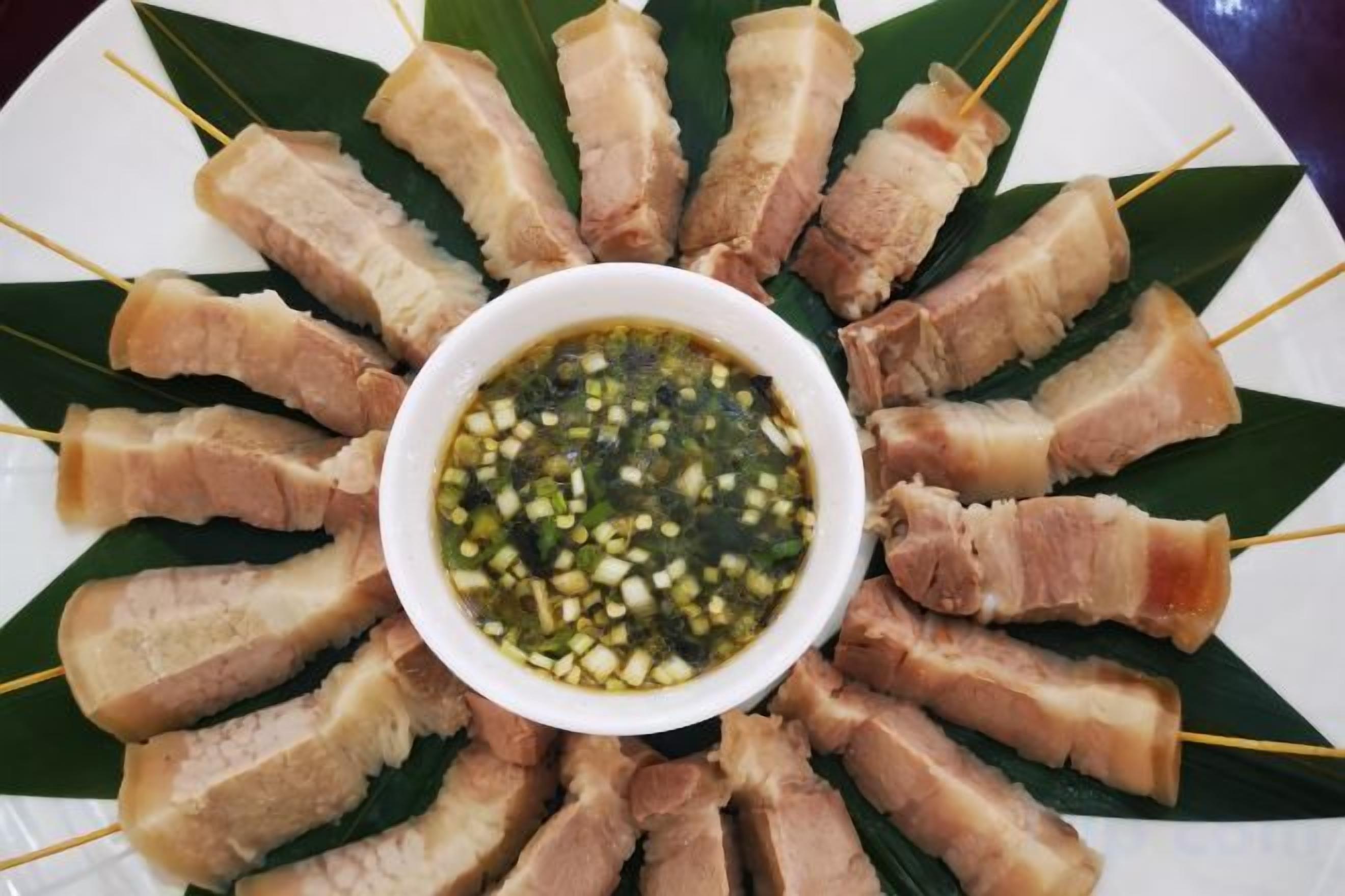 A plate of skewered pork belly arranged in a circular pattern with a bowl of dipping sauce in the center.
