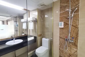 Un baño con mampara de vidrio, inodoro blanco, encimera negra con lavabo y zona de ducha con pared de mármol.