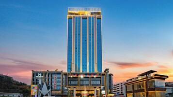A modern hotel with a tall central tower, a ground-level building with a glass facade, and a parking lot.