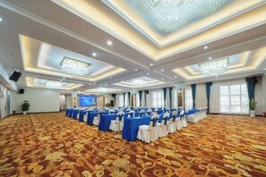 Un amplio salón de conferencias con filas de mesas y sillas, piso alfombrado y un techo alto con iluminación empotrada.